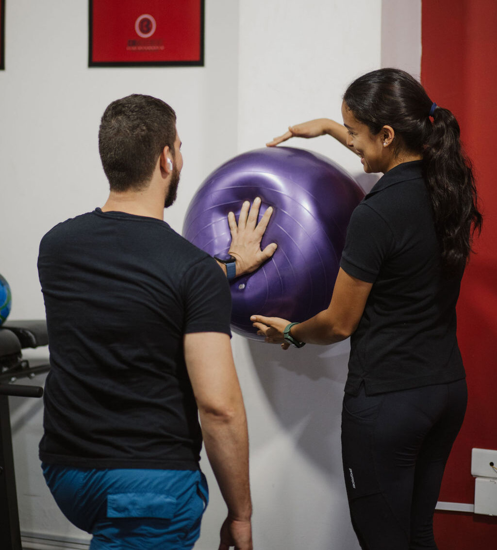 Paciente en recuperación Paciente presionando una bola de terapia contra la pared mientras la fisioterapeuta le ayuda